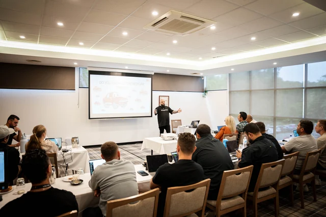 A wide view of a LaunchHub workshop with a presenter and participants seated at tables